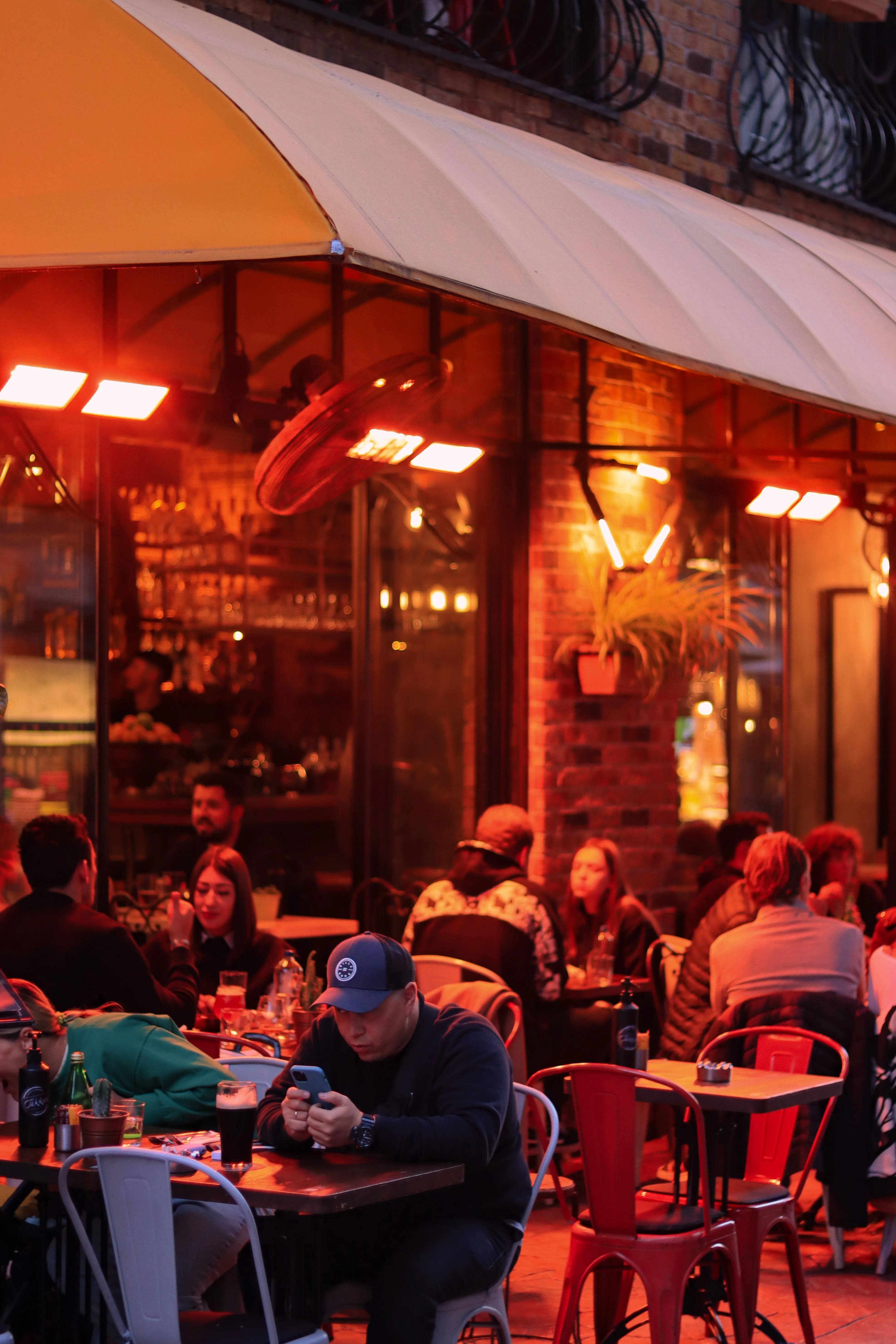 Terrasse de restaurant pleine en soirée — clients attablés sous un auvent, lumière chaude des chauffages de terrasse